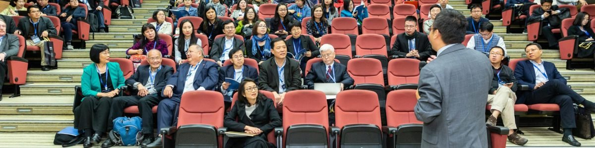 Professional setting of a business conference with attendees and a presenter in an auditorium.